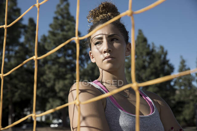 Portrait of woman behind football goal netting looking away — Stock Photo