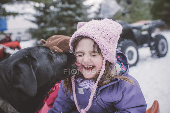 Young girl with dog in snowy landscape, dog licking girl's face — Stock Photo