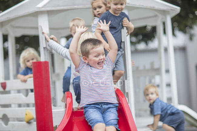 Мальчики и девочки в детском саду, катаются на горке по детской площадке — стоковое фото