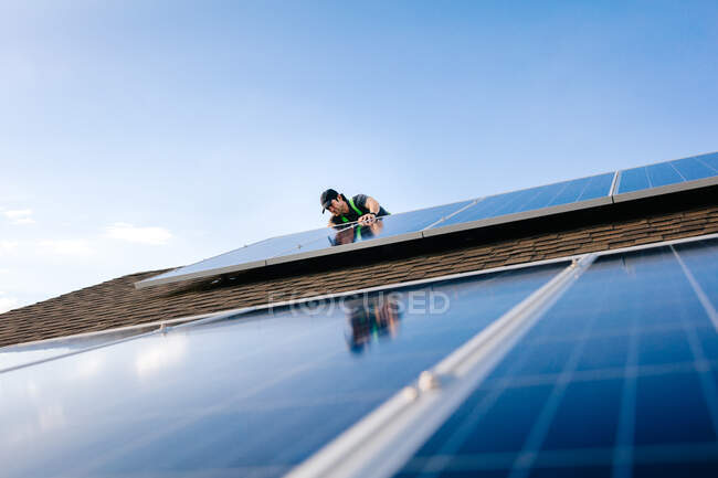 Workman instalación de paneles solares en el techo de la casa, vista de ángulo bajo - foto de stock