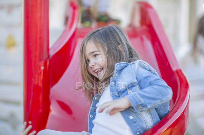 Chica en preescolar, deslizándose hacia abajo diapositiva en el jardín - foto de stock