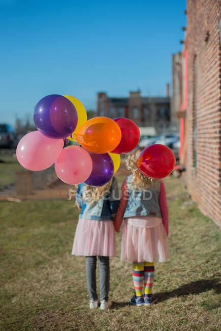 Two sisters holding hands with bunch of colourful balloons, rear view — Stock Photo