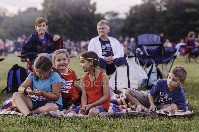 Группа взрослых и детей, сидящих на открытом воздухе, во время празднования 4 июля — стоковое фото
