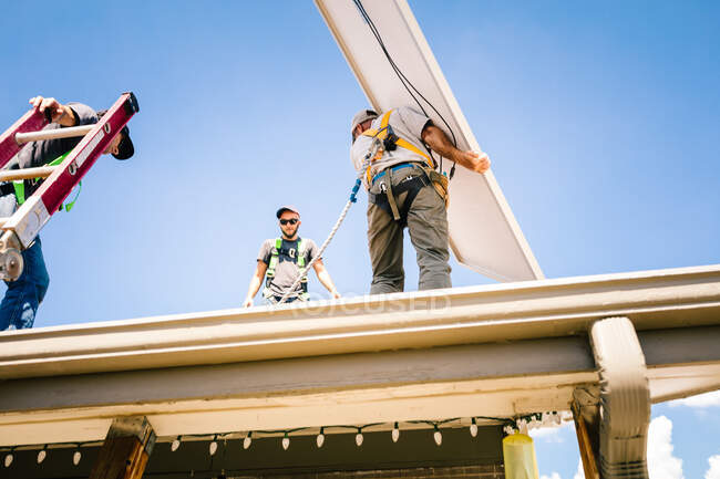Workmen preparing to install solar panel on roof of house, low angle view — Stock Photo