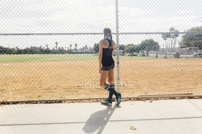 Schoolgirl soccer player at wire fence on school sports field — Stock Photo
