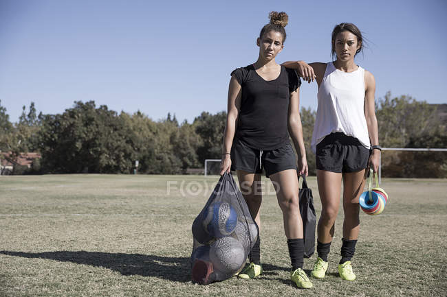 Retrato de mujeres en campo de fútbol con balones de fútbol en saco neto - foto de stock