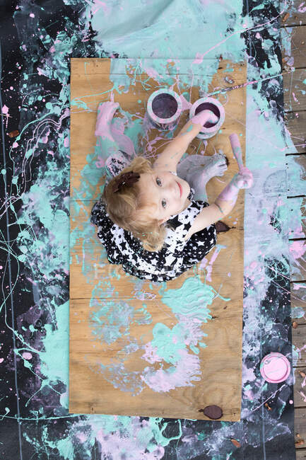 Visão aérea da menina coberta de tinta sentada na pintura olhando para cima — Fotografia de Stock