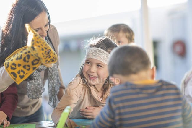 Mulher adulta média, vestindo fantoche de mão, de pé ao lado de crianças, rindo — Fotografia de Stock