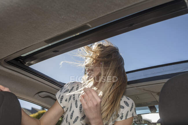 Jeune femme en voiture, regardant par le toit ouvrant — Photo de stock