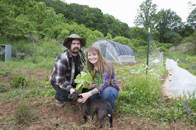 Couple with dog in vegetable garden looking at camera smiling — Stock Photo