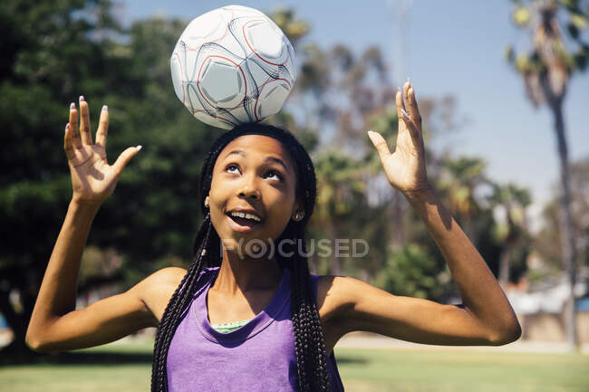 Adolescente colegiala jugador de fútbol balanceo pelota en la cabeza en el campo de deportes de la escuela - foto de stock