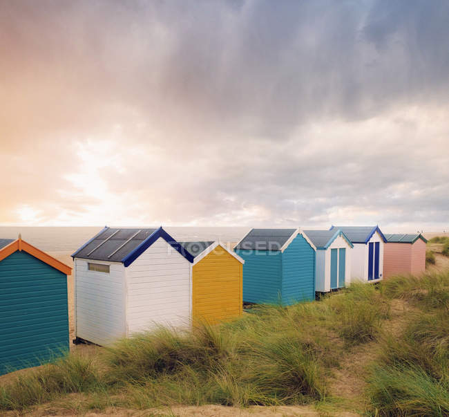 Fila de coloridas cabañas de playa y nubes de tormenta sobre el mar, Southwold, Suffolk, Inglaterra - foto de stock