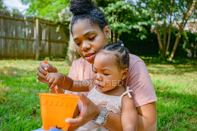 Середня доросла жінка грає з іграшковим відром у саду з дочкою — стокове фото