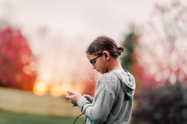 Vista lateral da menina com fones de ouvido e smartphone no jardim — Fotografia de Stock