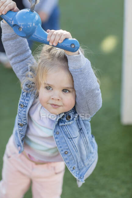 Chica en preescolar, sosteniendo columpio de cuerda de patio en el jardín - foto de stock