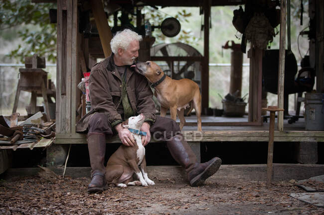 Hombre con perros de compañía por cabaña de trabajo de madera - foto de stock