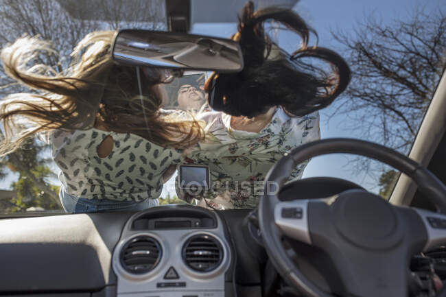 Deux femmes allongées sur le capot de la voiture, vues de l'intérieur de la voiture — Photo de stock