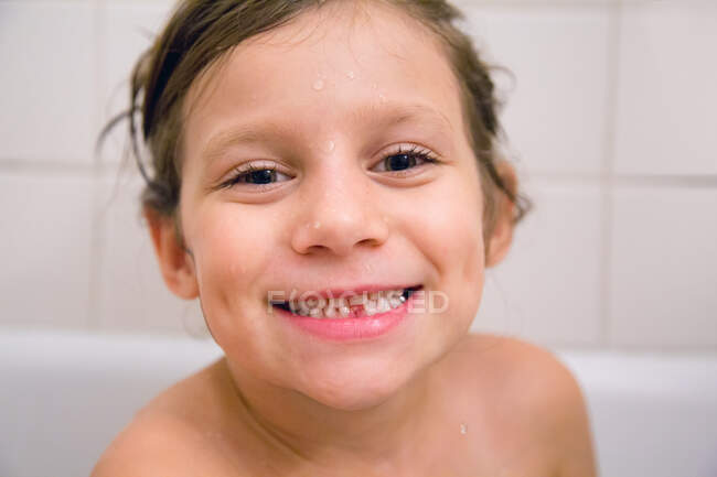 Retrato de chica con diente perdido en el baño, mirando a la cámara sonriendo - foto de stock
