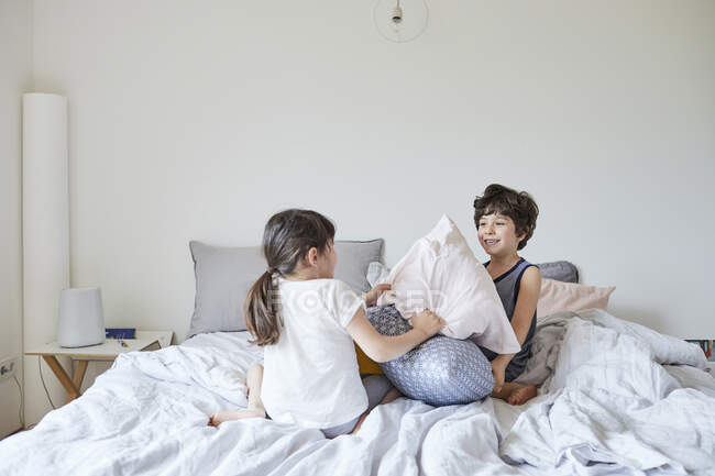 Брат и сестра дерутся подушками на кровати — стоковое фото