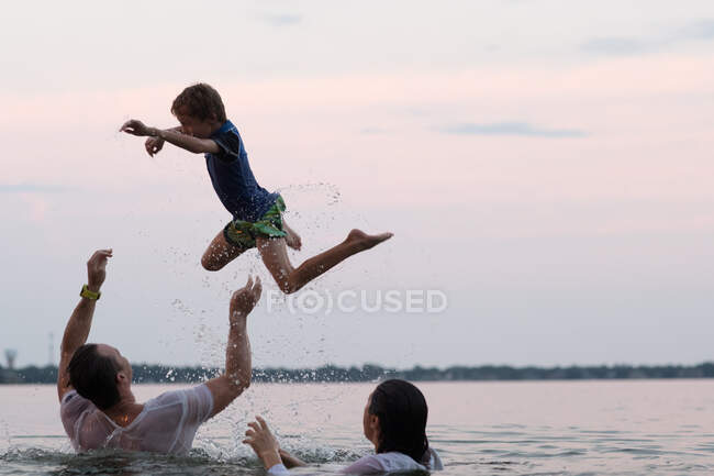 Одягнені батьки в воду кидають сина в повітрі, Дестін (штат Флорида, США). — стокове фото