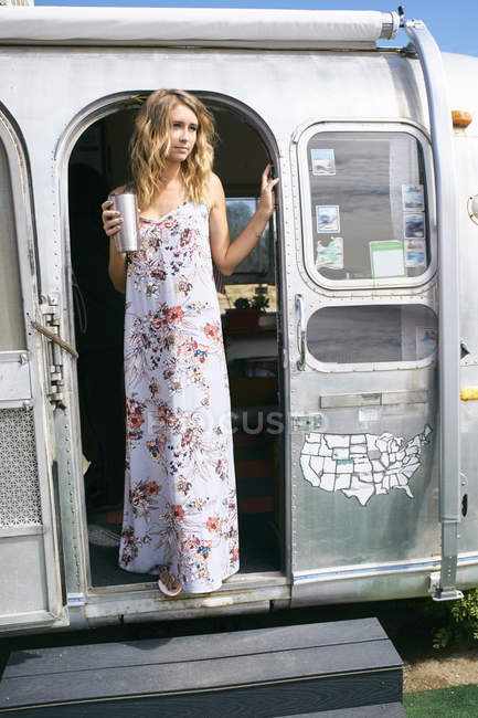 Young woman wearing maxi dress gazing from airstream doorway — Stock Photo