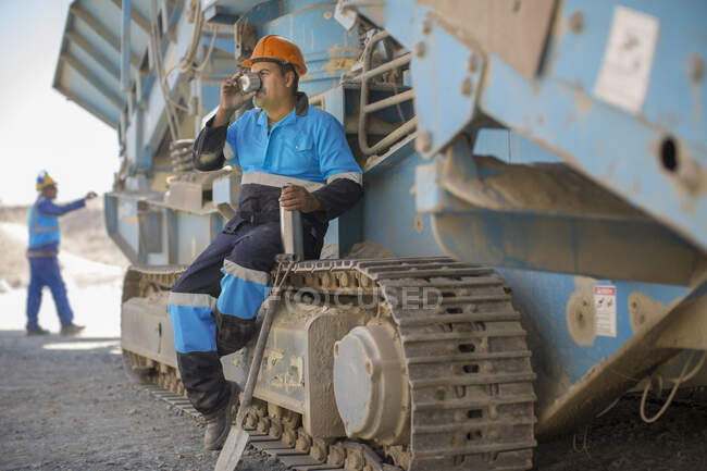 Trabalhador da pedreira descansando em máquinas pesadas, bebendo de copo de frasco — Fotografia de Stock