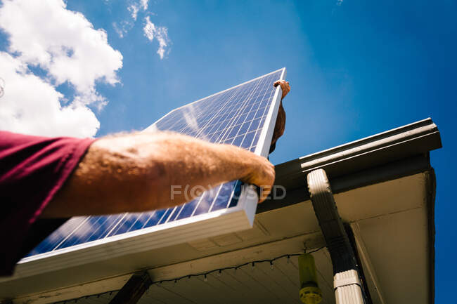 Workman elevando el panel solar a su colega de pie en el techo, vista de ángulo bajo, primer plano - foto de stock