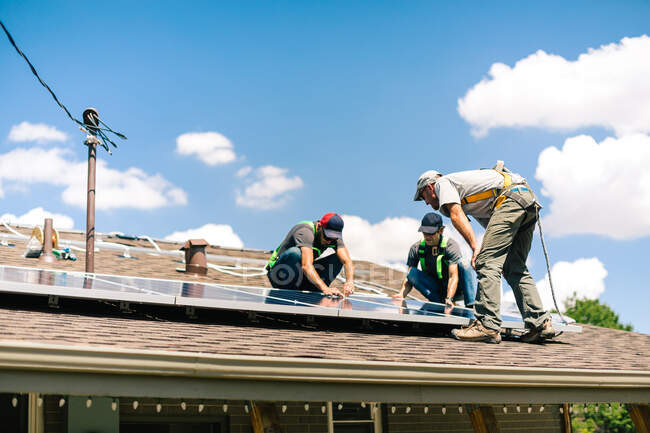 Tres trabajadores instalando paneles solares en el techo de la casa, vista de ángulo bajo - foto de stock