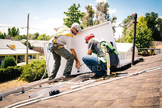 Двоє робітників встановлюють сонячні панелі на даху будинку — стокове фото
