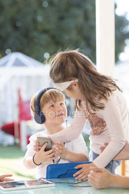 Dos niños pequeños sosteniendo el teléfono inteligente, niño usando auriculares - foto de stock