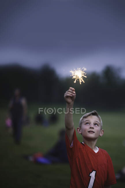 Boy with arm raised holding sparkler — Stock Photo