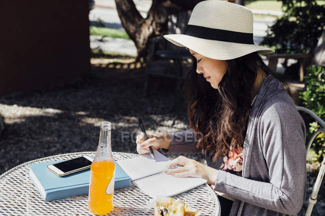 Jeune femme assise à l'extérieur, écrivant dans un cahier — Photo de stock