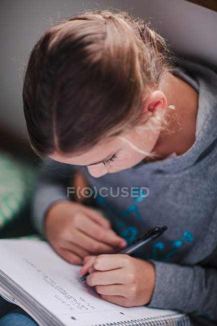 Chica en el suelo concentrándose en la escritura de la tarea - foto de stock