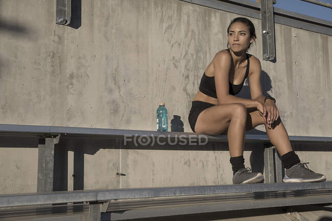 Портрет женщины в спортивной одежде, сидящей на скамейке и смотрящей в сторону — стоковое фото