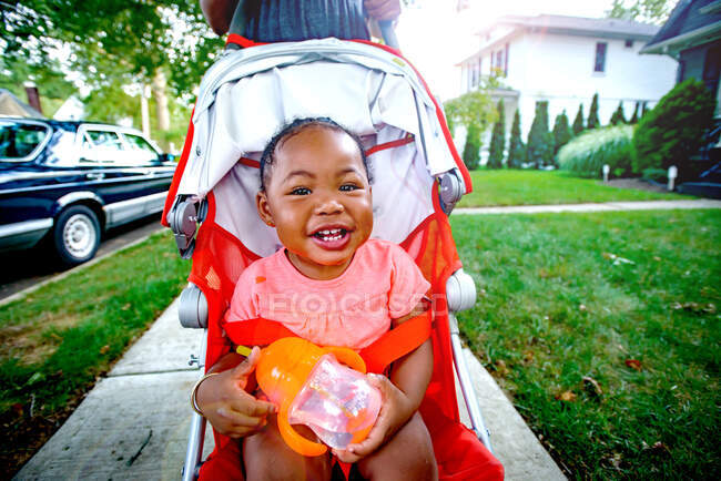 Happy baby girl in pushchair on suburban sidewalk, portrait — Stock Photo