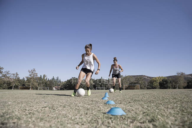 Dos mujeres jóvenes regateando balones de fútbol - foto de stock