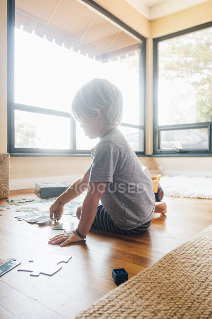 Niño sentado en el suelo haciendo rompecabezas - foto de stock