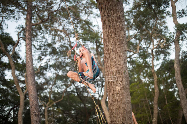 Rapaz balançando na corda na árvore — Fotografia de Stock