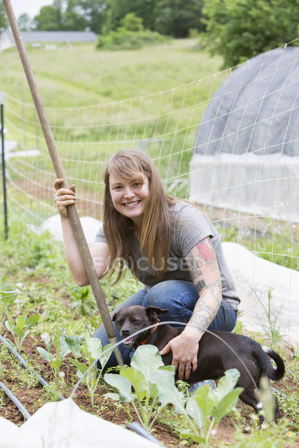Donna con cane che sorride alla macchina fotografica nell'orto — Foto stock