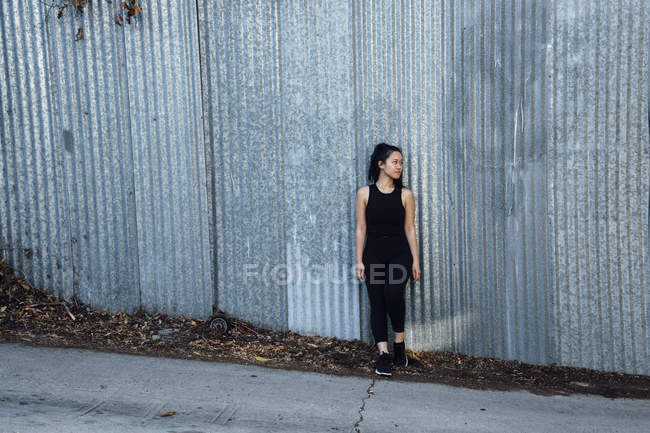 Portrait of young woman standing in front of corrugated fencing — Stock Photo