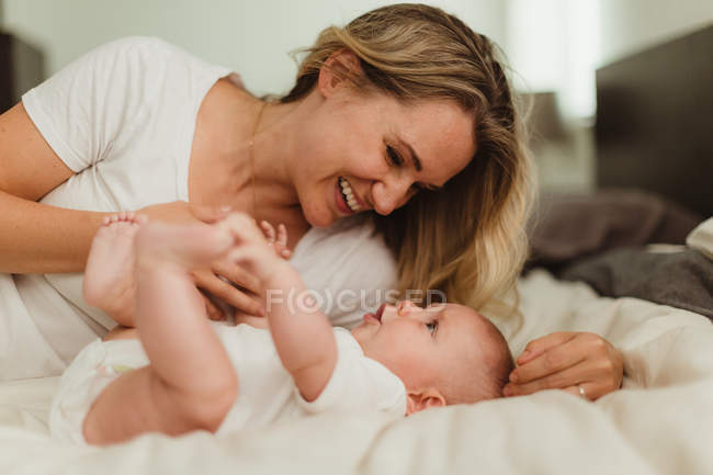 Жінка лежить на ліжку грає з дочкою — стокове фото