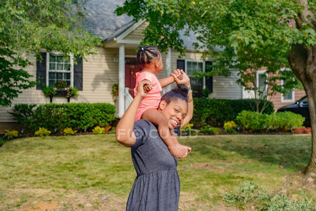 Mujer adulta en el jardín llevando a la hija del bebé en hombros, retrato - foto de stock