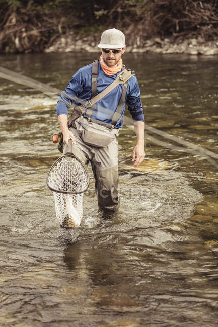 Giovane pescatore inginocchiato nel fiume che trasporta pesce pescato in rete, Mozirje, Brezovica, Slovenia — Foto stock