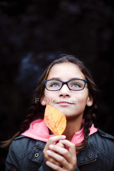 Portrait of girl with plaits and glasses holding leaf — Stock Photo