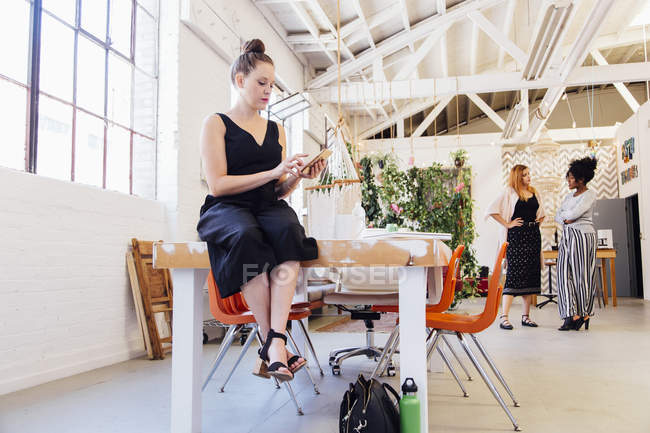 Женщина сидит на столе в промышленном офисном здании и использует смартфон — стоковое фото