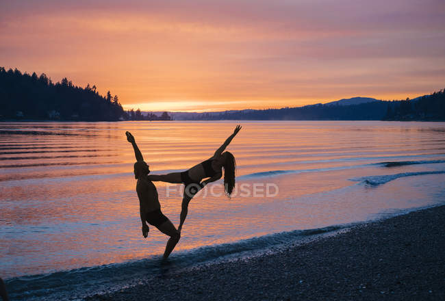 Couple practising yoga on beach at sunset — Stock Photo