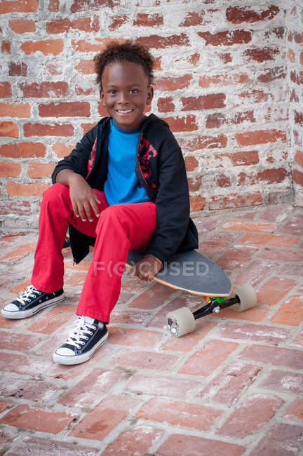 Portrait de jeune garçon assis sur skateboard — Photo de stock
