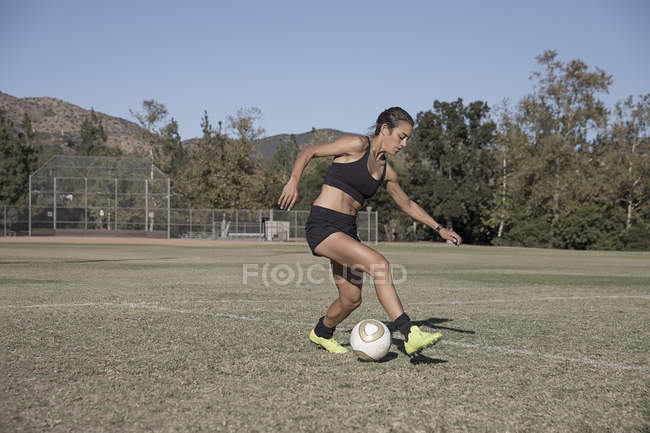 Jeune femme sur le terrain de football jouant au football — Photo de stock