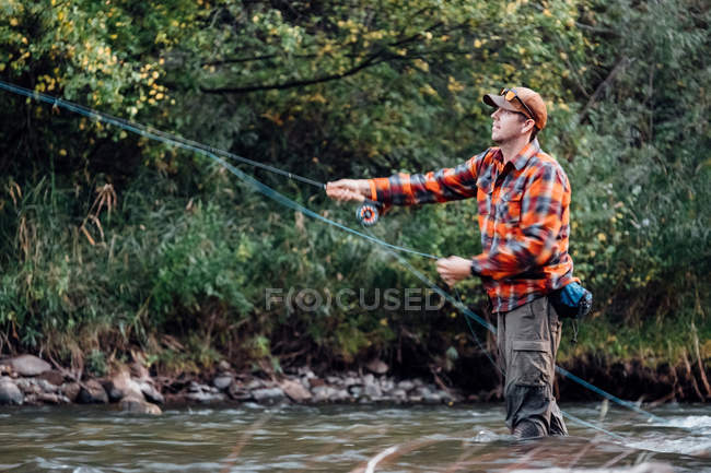 Side view of man wading in river with fishing rod — Stock Photo