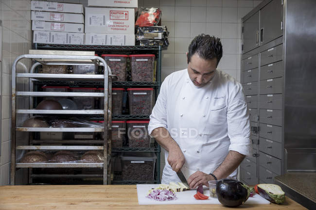 Chef in commercial kitchen slicing aubergine — Stock Photo